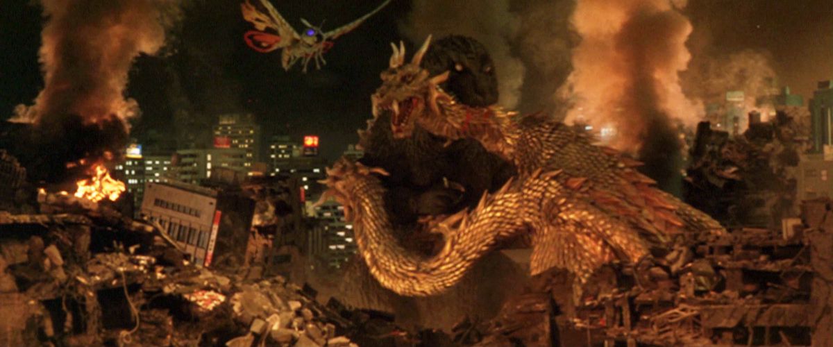 Godzilla biter nacken på kung Ghidorah med en förstörd stad i bakgrunden och Mothra flyger mot dem.