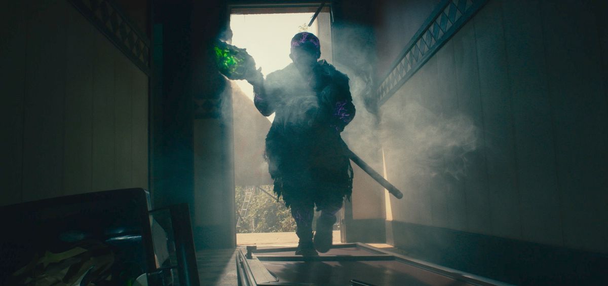 Peter Dinklage som Toxie i The Toxic Avenger, höljd i skugga och håller en kristallgrön stav medan han går genom en dörröppning