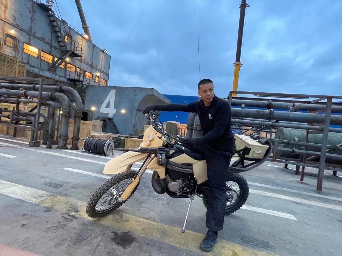 Stuntkoordinatorn Alan Ng sitter på en motorcykel med maskingevär på en båt på uppsättningen av Expend4bles.