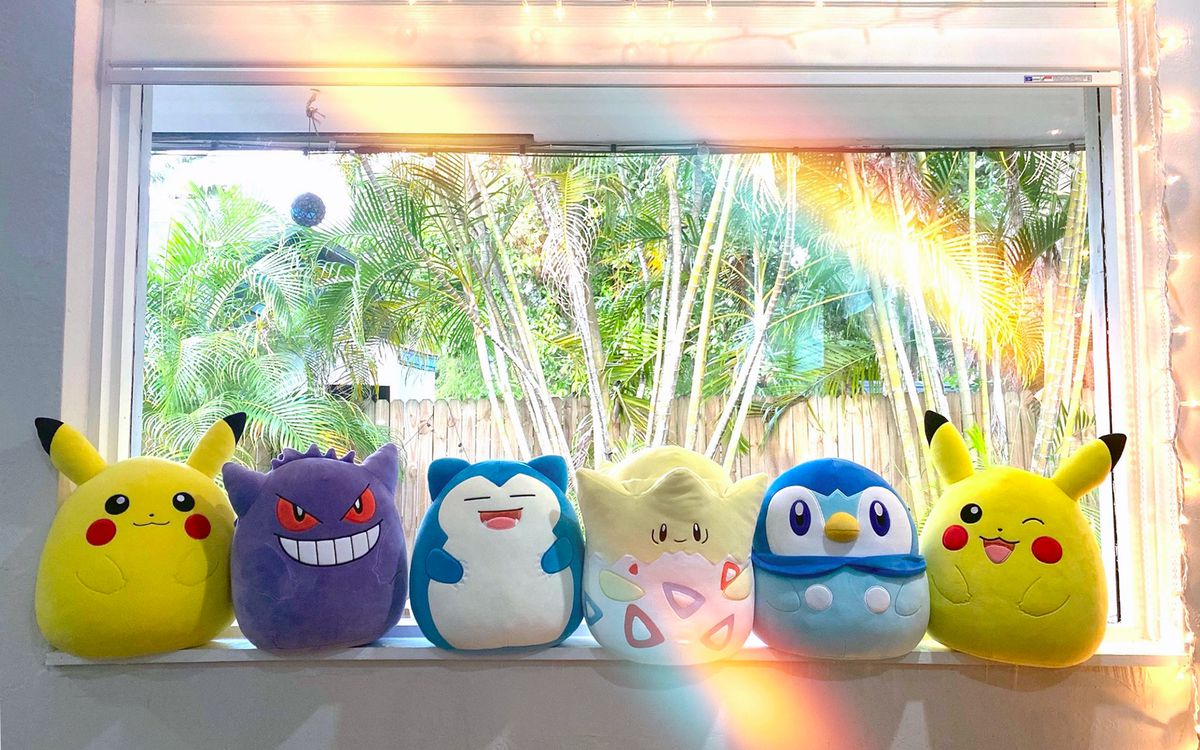 En serie Pokémon Squishmallows (Pikachu, Gengar, Snorlax, Togepi, Piplup och en blinkande Pikachu) sitter på en fönsterbräda