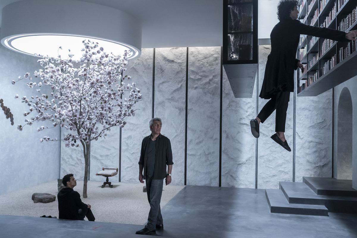 En man svävar mot en bokhylla monterad i taket i en modern extralägenhet när två män tittar på framför ett körsbärsträd i AMC:s Intervju med vampyren.