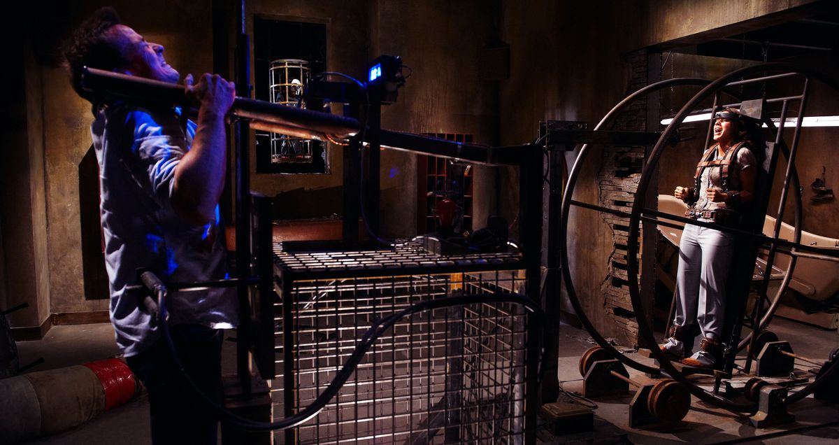 A man heaves two poles upward at one end of one of Jigsaw’s complicated machine traps as a woman tied into a different part of the machine screams in Saw 3D