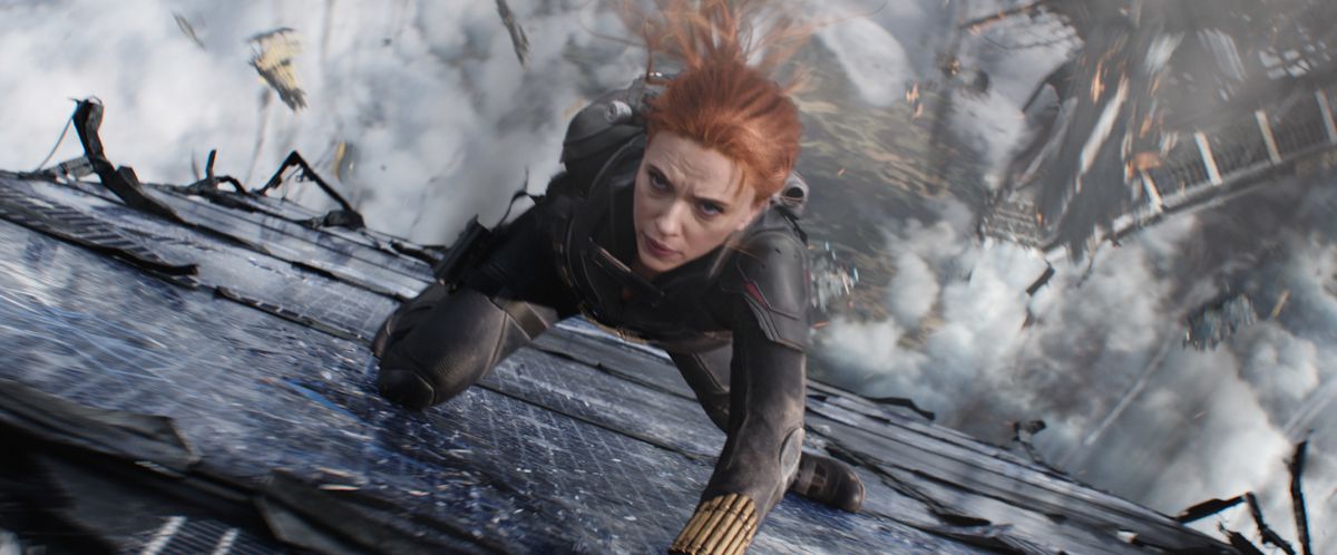 Black Widow slides her way down the side of a building amid falling debris in the Marvel Studios film Black Widow.