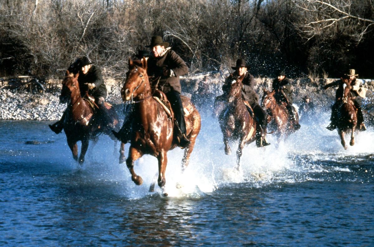 En grupp cowboys på hästar korsar en flod i Silverado