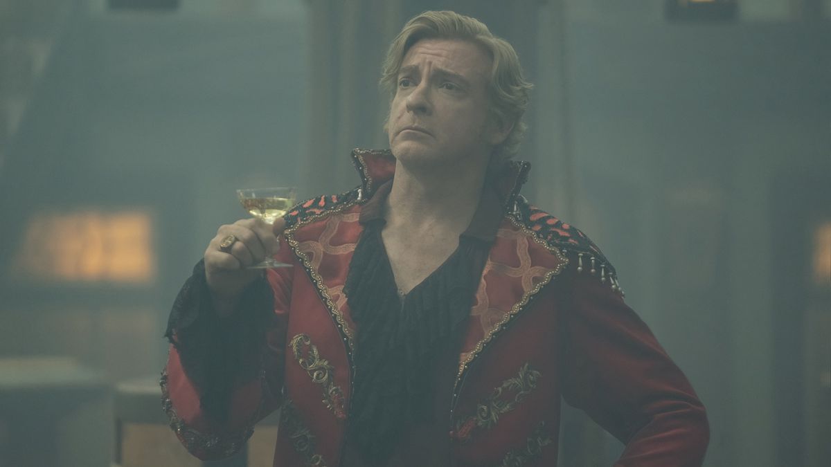 Stede Bonnet (Rhys Darby) poserar med en cocktail och ser självgod ut i en klibbig, rickrackklädd röd sidenjacka i säsong 2 av Our Flag Means Death
