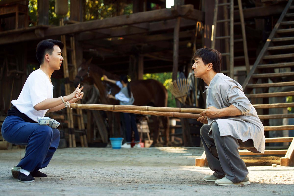Jackie Chan och Kevin Guo utför ansträngande hukövningar när en häst står i bakgrunden i Ride On.