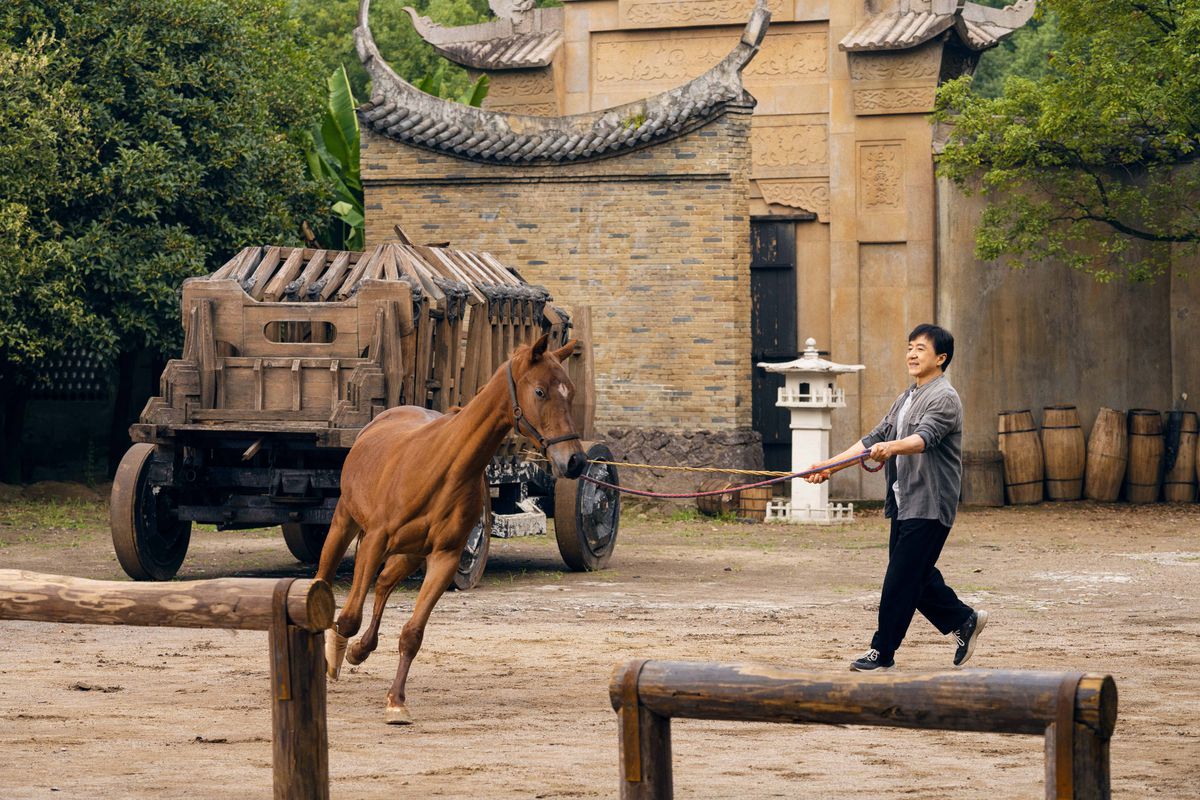En häst galopperar runt ett öppet område medan Jackie Chan instruerar i Ride On.