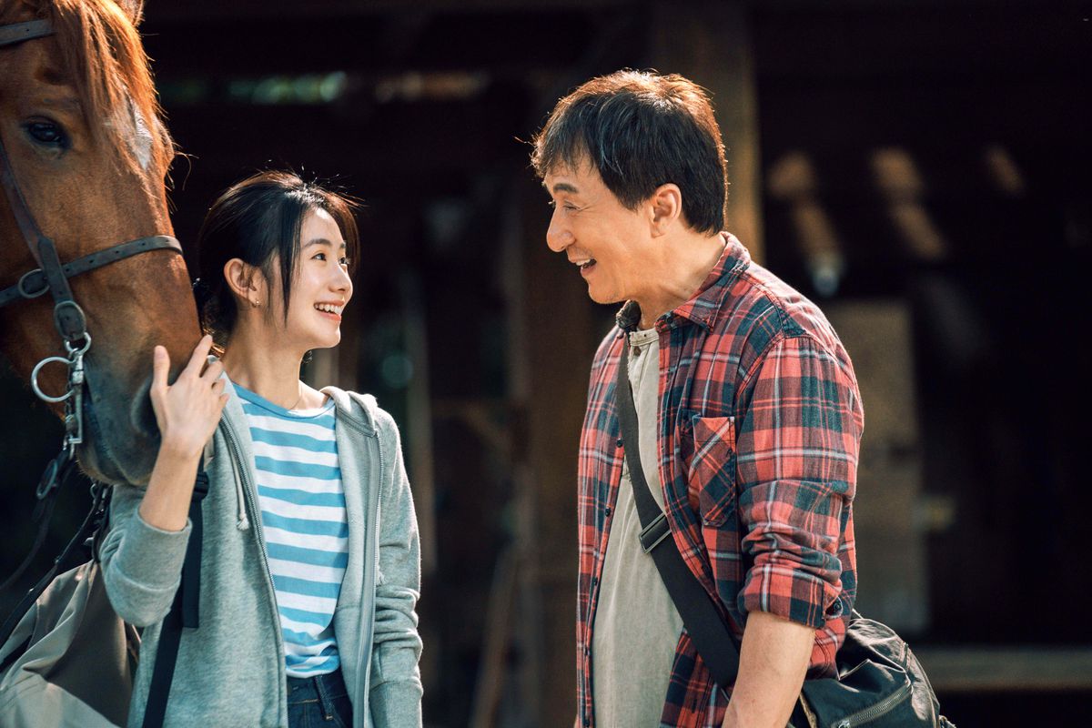 Jackie Chan och Haocun Liu ler mot varandra när hon håller en hästs nosparti i Ride On.