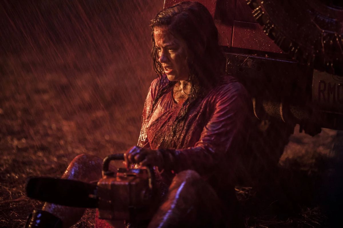 Jane Levy som Mia Allen håller en motorsåg när hon sitter på marken, hennes kläder dränkta av regn och inälvor i 2013 års Evil Dead.