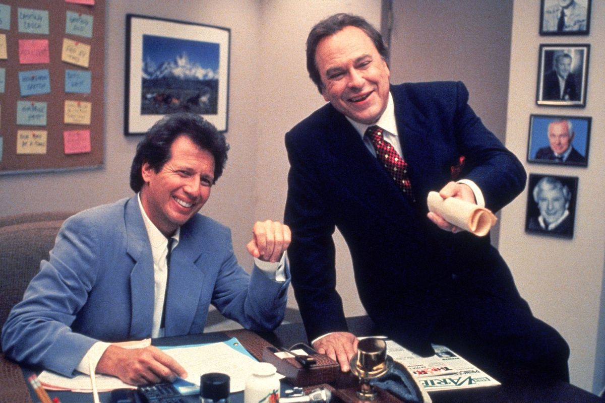 Garry Shandling and Rip Torn smile on a cluttered desk in The Larry Sanders Show.