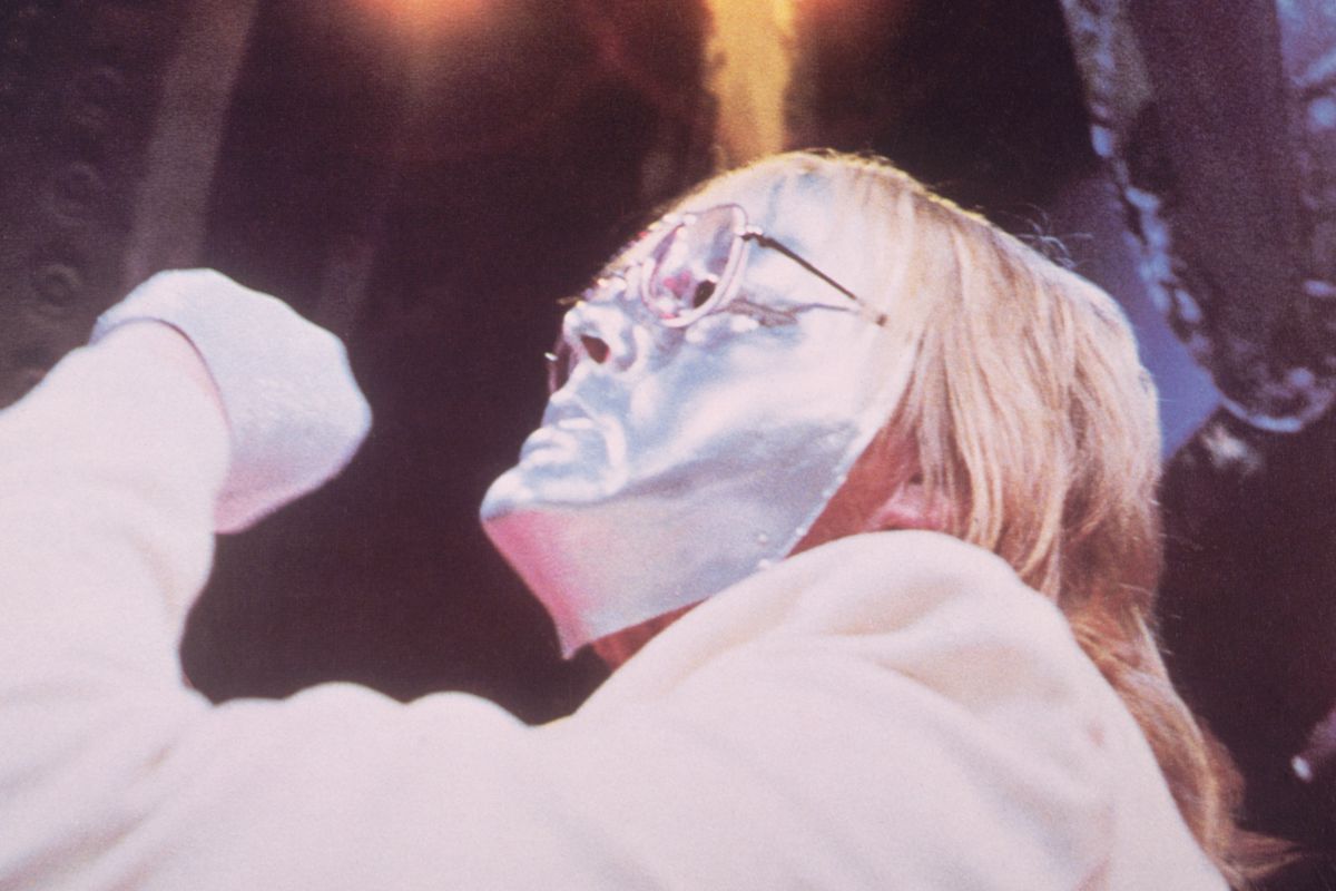 Paul Williams, klädd i en silverfärgad ansiktsmask med glasögonen på masken, bältar ut sitt rockoperahjärta i Phantom of the Paradise från 1974.