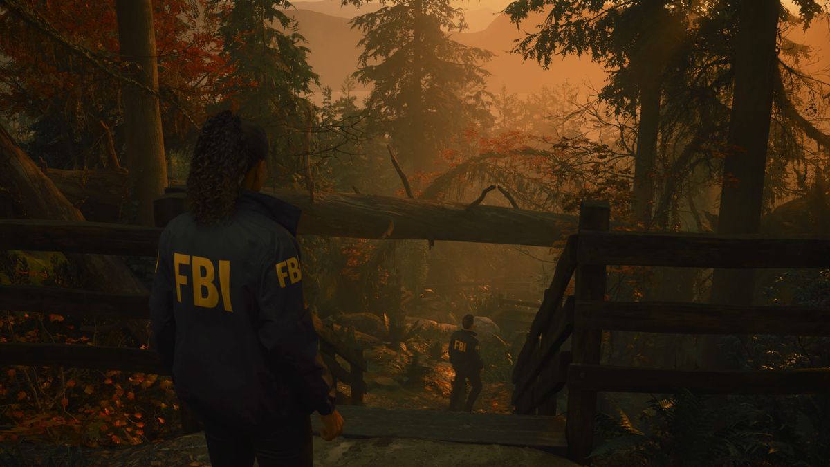 FBI-agenten Saga Anderson följer sin partner Alex Casey nerför en brant skogsstig i Alan Wake 2, med en vacker solnedgång i bakgrunden