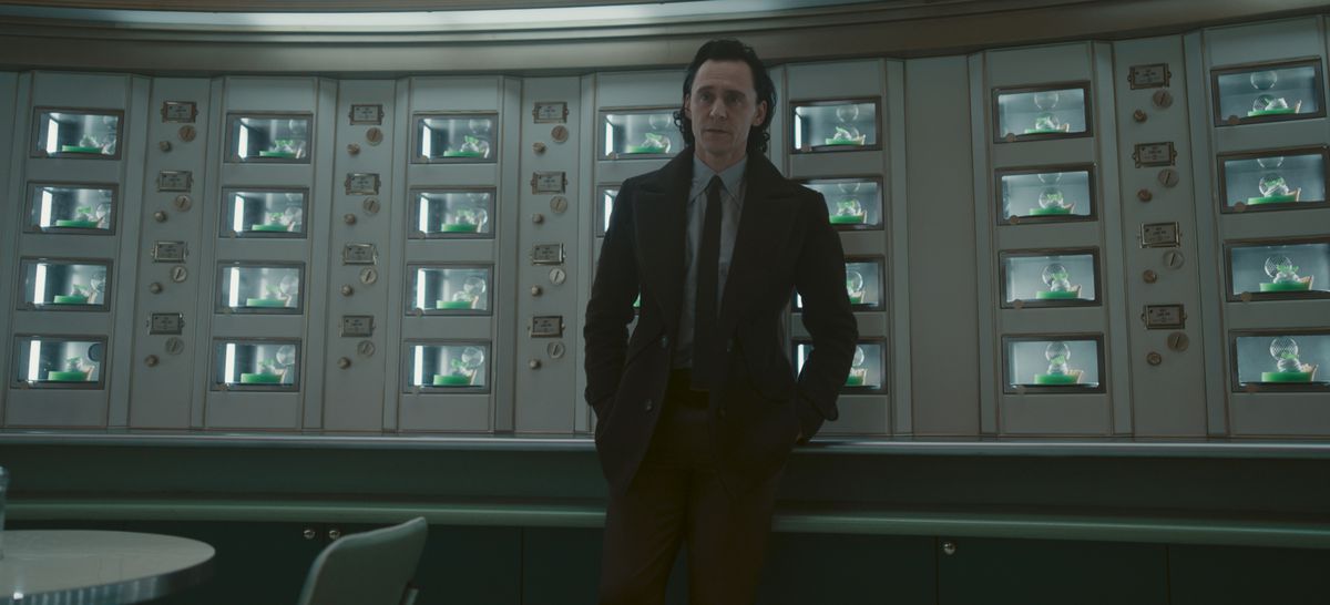 Loki (Tom Hiddleston) står mot en massa skärmar med händerna i fickorna