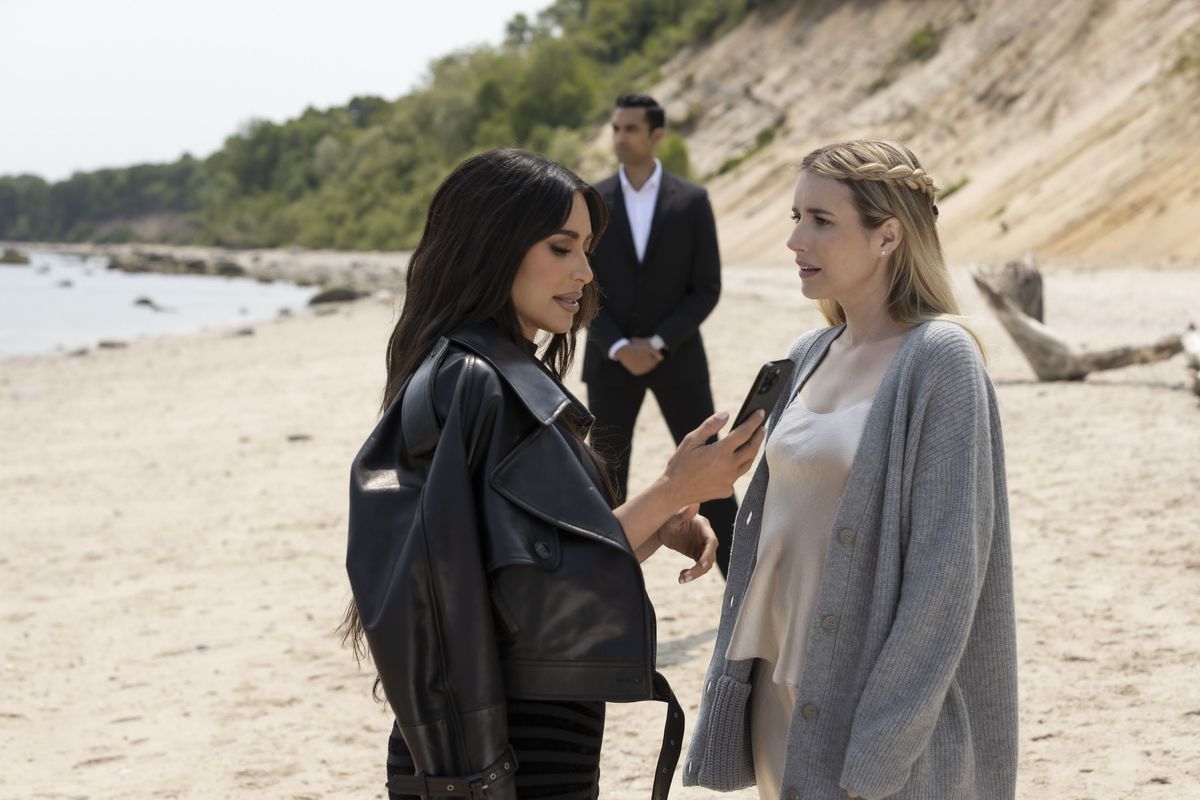 Kim Kardashian och Emma Roberts i AHS, står på en strand tillsammans, medan en livvakt tittar på
