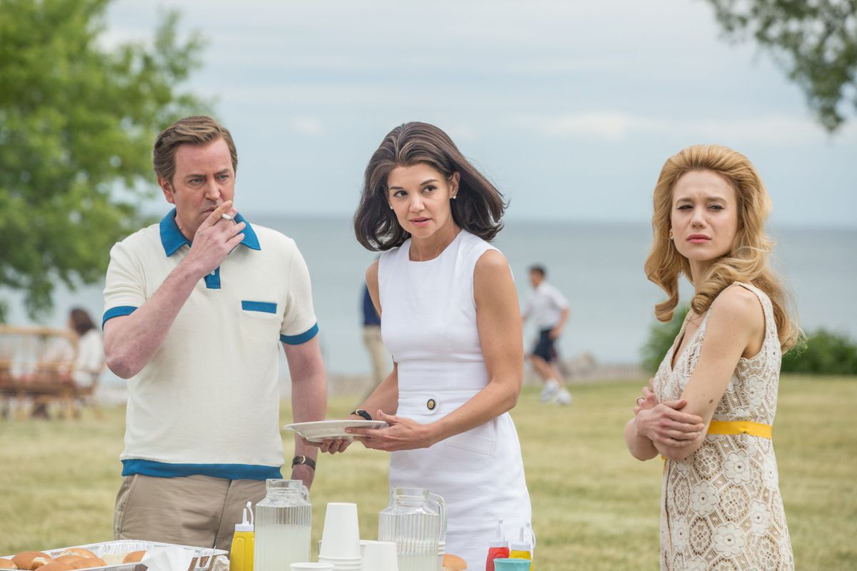 Ted Kennedy (Matthew Perry) röker bredvid två kvinnor som står nära ett matbord.  De tittar alla på något utanför skärmen