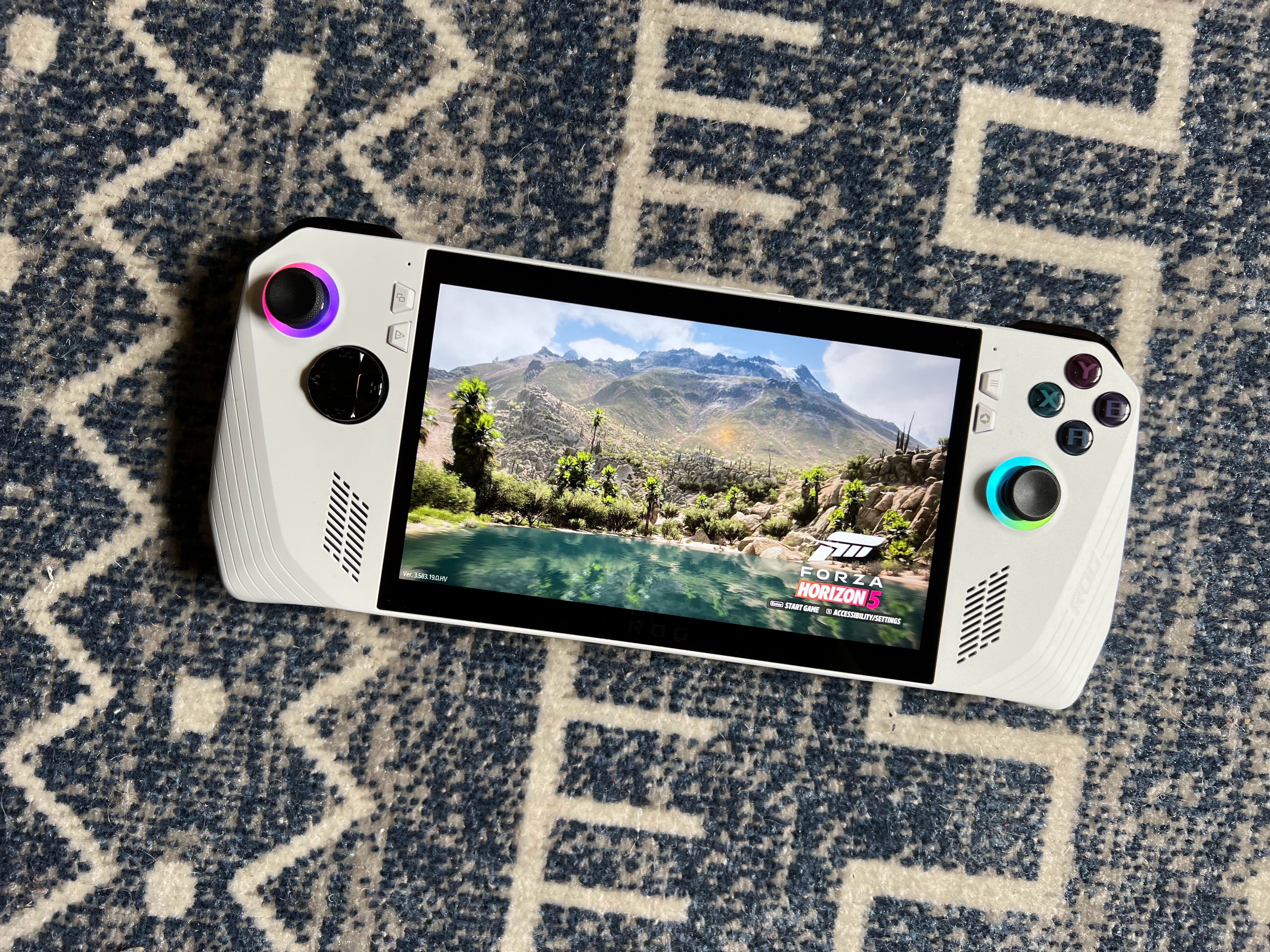 en sjö i bergen i Forza Horizon 5 körs på en Asus ROG Ally gaming handenhet, liggande på en blågrå matta, fotograferad från ovan