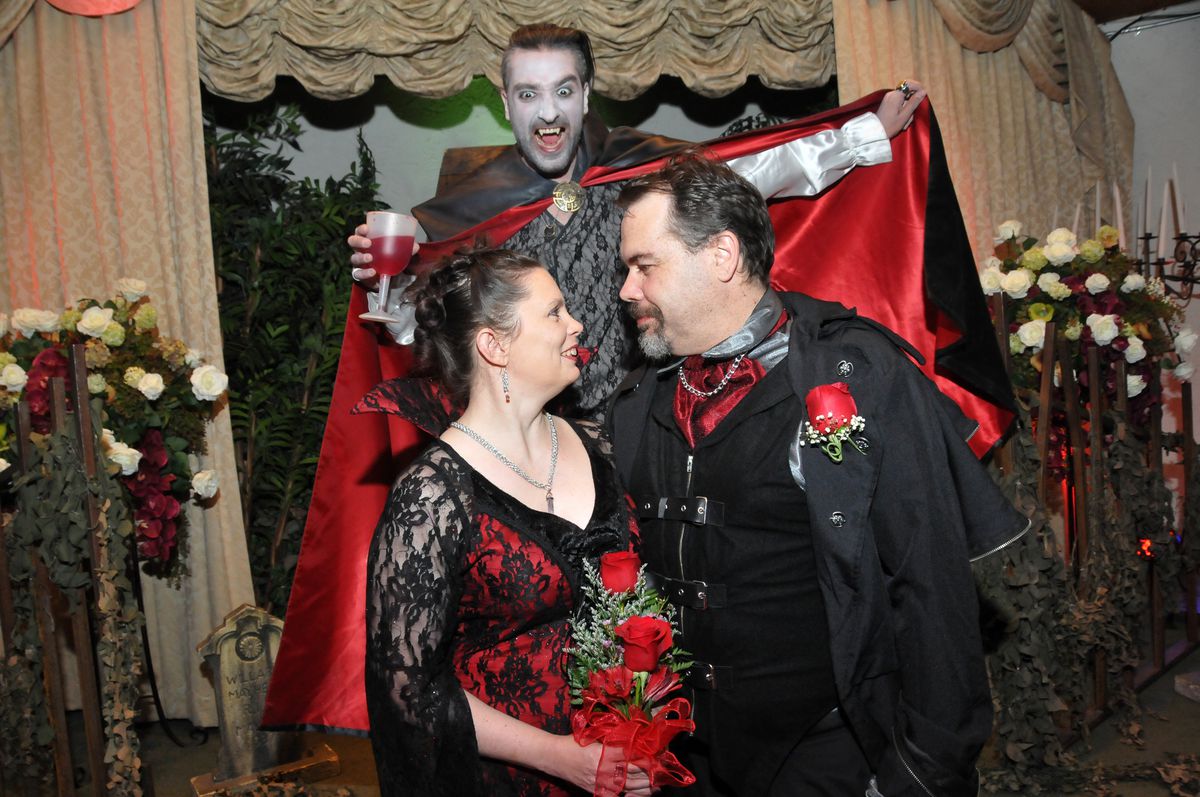 Två personer tittar in i varandras ögon vid en ceremoni för förnyelse av bröllopslöfte medan någon klädd som en vampyr skymtar bakom dem
