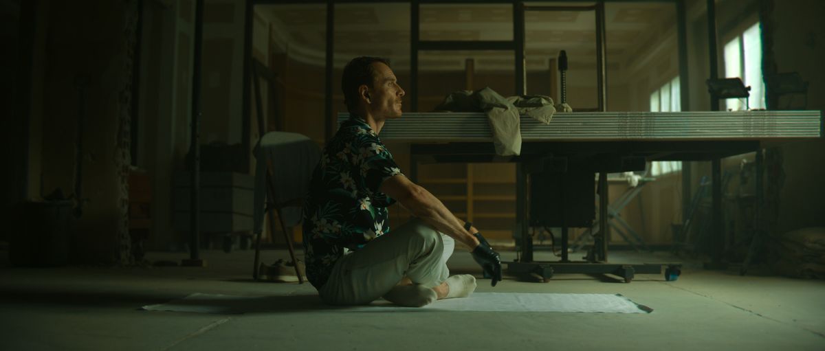 Michael Fassbender som Mördaren sitter med benen i kors på golvet på en plastduk