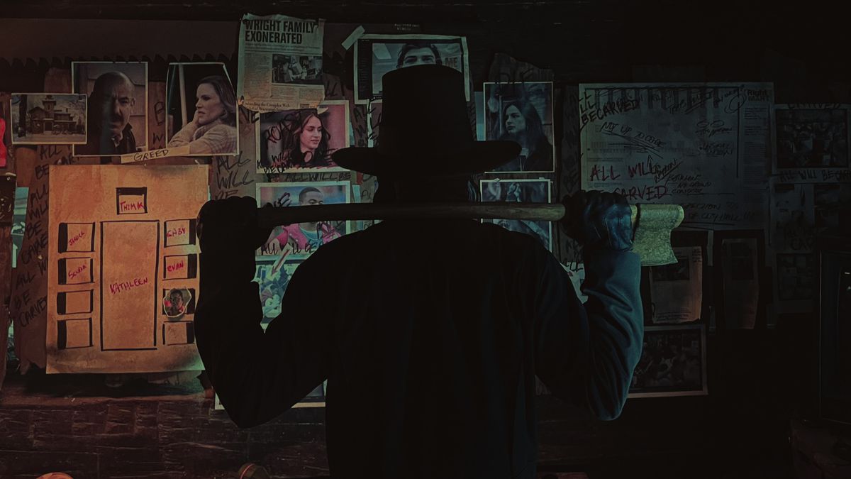 En man i hatt som håller en yxa står inför en vägg täckt av foton från filmen Thanksgiving