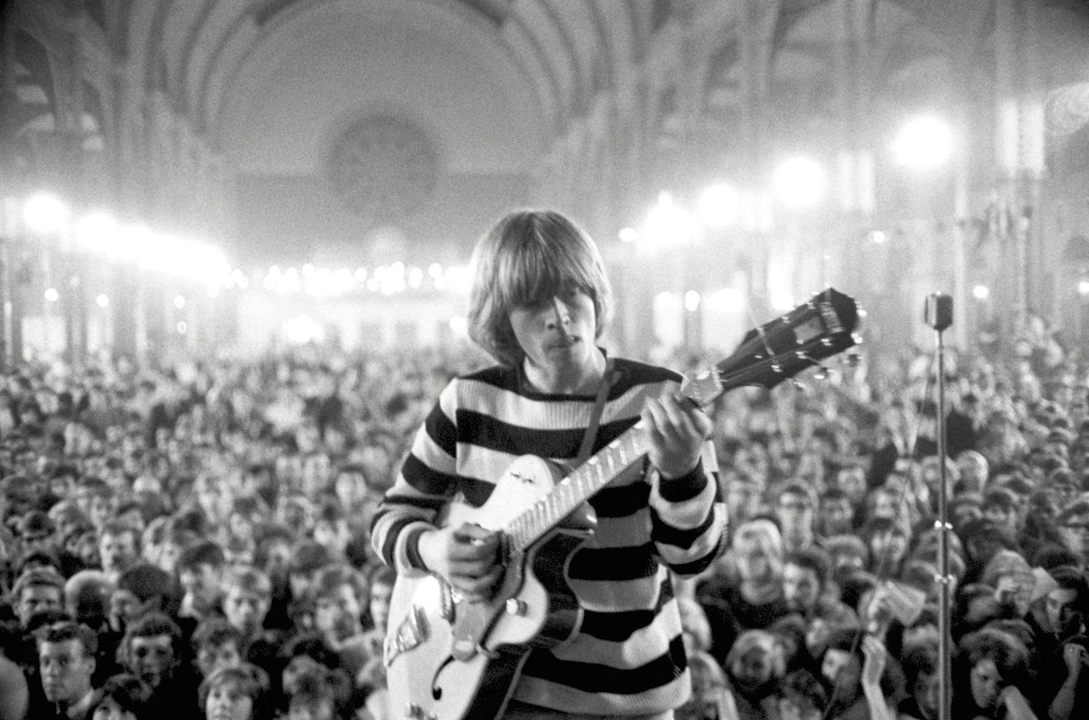 Photo of Brian Jones in front of a packed theater playing the guitar in The Stones & Brian Jones.