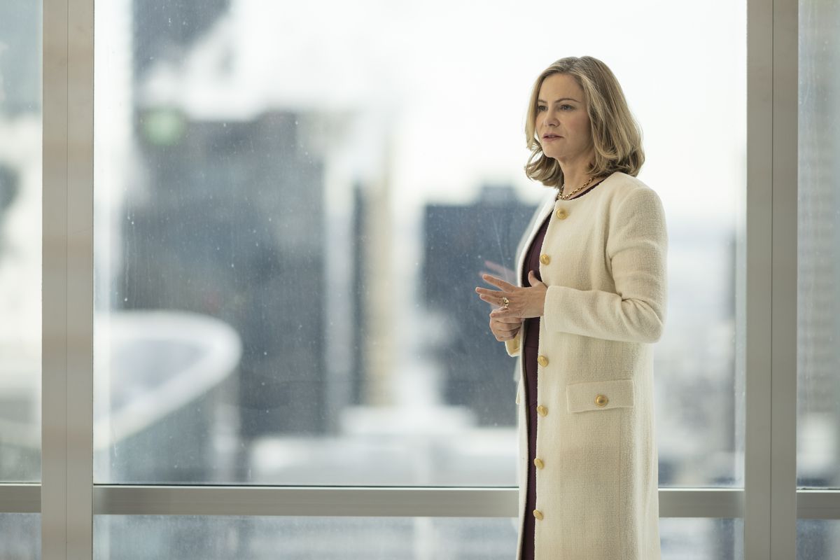 Jennifer Jason Leigh som Lorraine Lyon står i en dyr vit rock framför ett kontorsfönster i FX:s Fargo säsong 5.