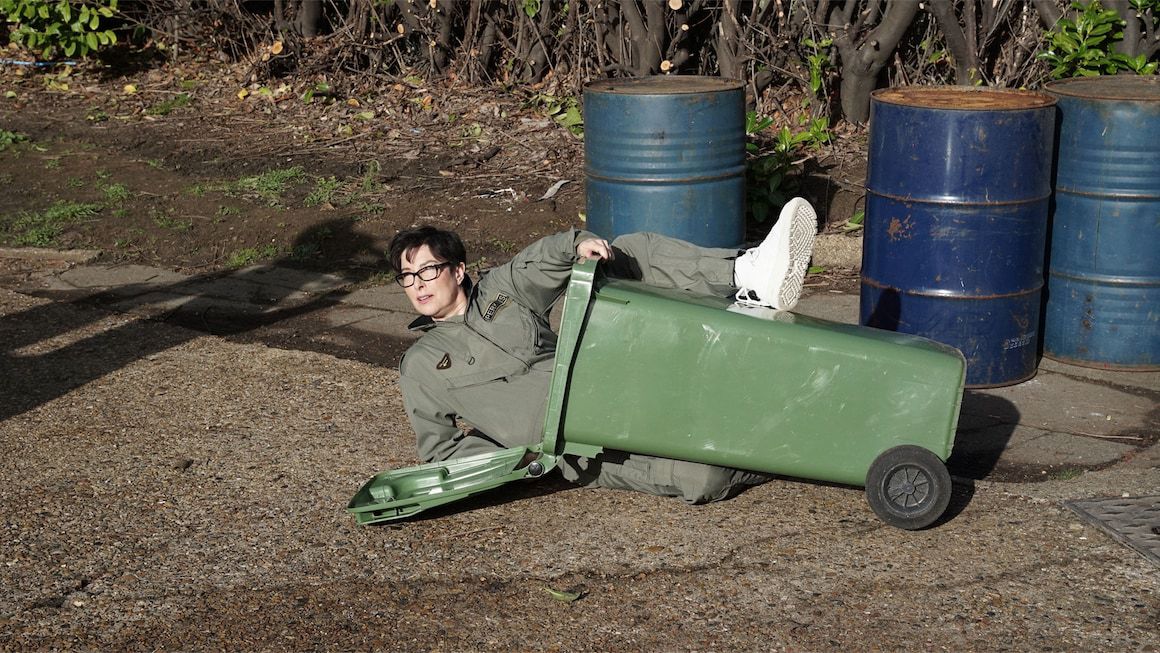 Sue Perkins holds a trash can between her legs while lying on the ground in Taskmaster