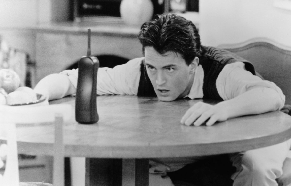 Chandler (Matthew Perry) sitter med huvudet på ett bord och tittar desperat på en telefon
