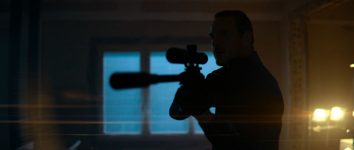 Michael Fassbender som en lönnmördare som riktar ett prickskyttegevär genom ett fönster i The Killer.