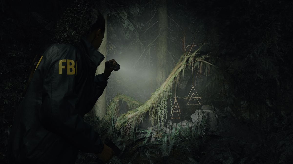 Saga Anderson håller i en ficklampa för att undersöka ett konstigt par trädekorationer som hänger från en mörk skogsgren i Alan Wake 2.