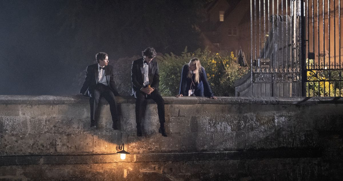 Oliver (Barry Keoghan) och Felix Catton (Jacob Elordi), i smoking, sitter tillsammans på en liten stenbro över en damm med Venetia (Alison Oliver) stående i närheten i Saltburn