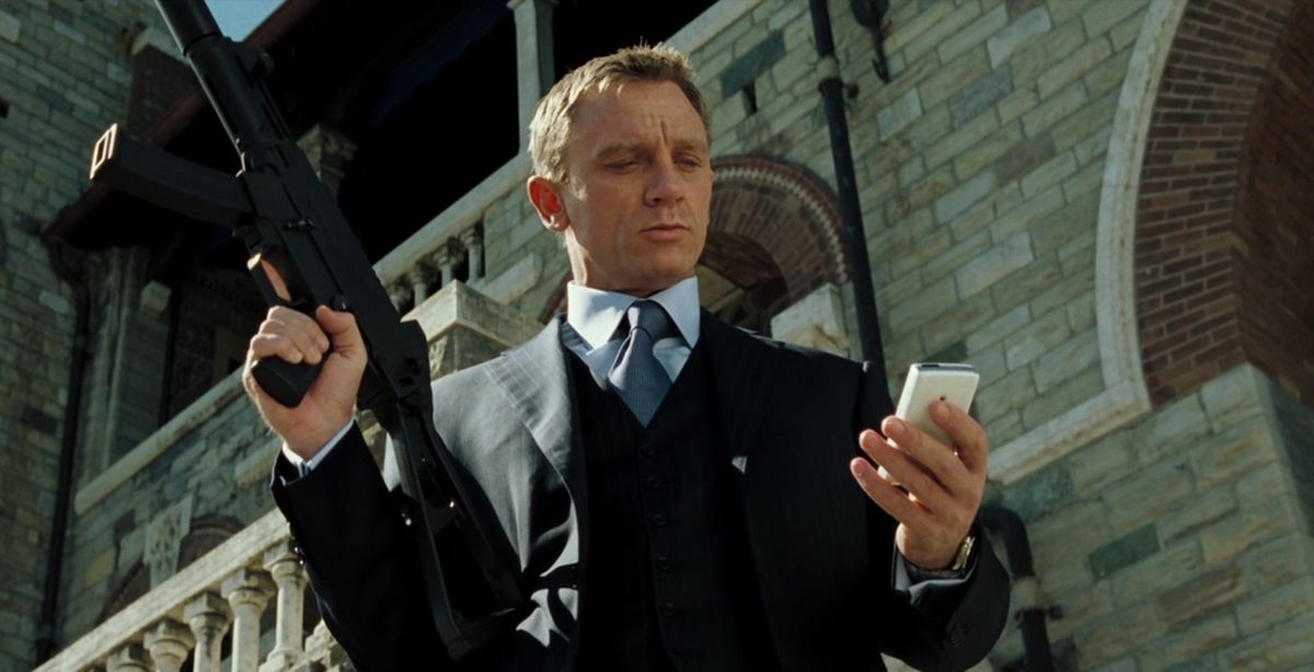 Daniel Craig som James Bond i Casino Royale, klädd i kostym och kollar sin telefon medan han håller en pistol