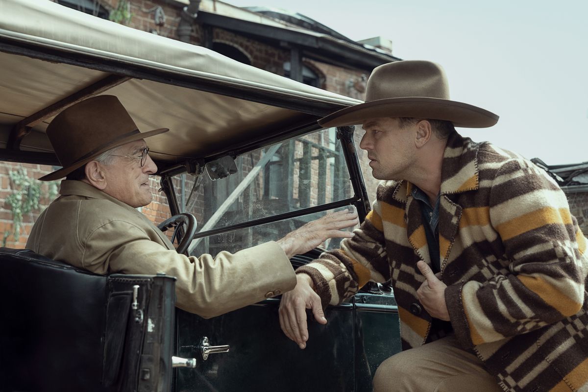 Leonardo DiCaprio i cowboyhatt och poncho lutar sig över en bil som körs av Robert DeNiro i Killers of the Flower Moon.