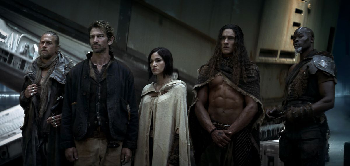 En gruppbild från Rebel Moon Part One: A Child of Fire, som ser lite ut som en Dune-cosplaygrupp, med alla i smutsiga, misshandlade, jordnära retrofuturistiska kläder eller rustningar.  Charlie Hunnam som Kai, Michiel Huisman som Gunnar, Sofia Boutella som Kora, Staz Nair som Tarak och Djimon Hounsou som Titus.