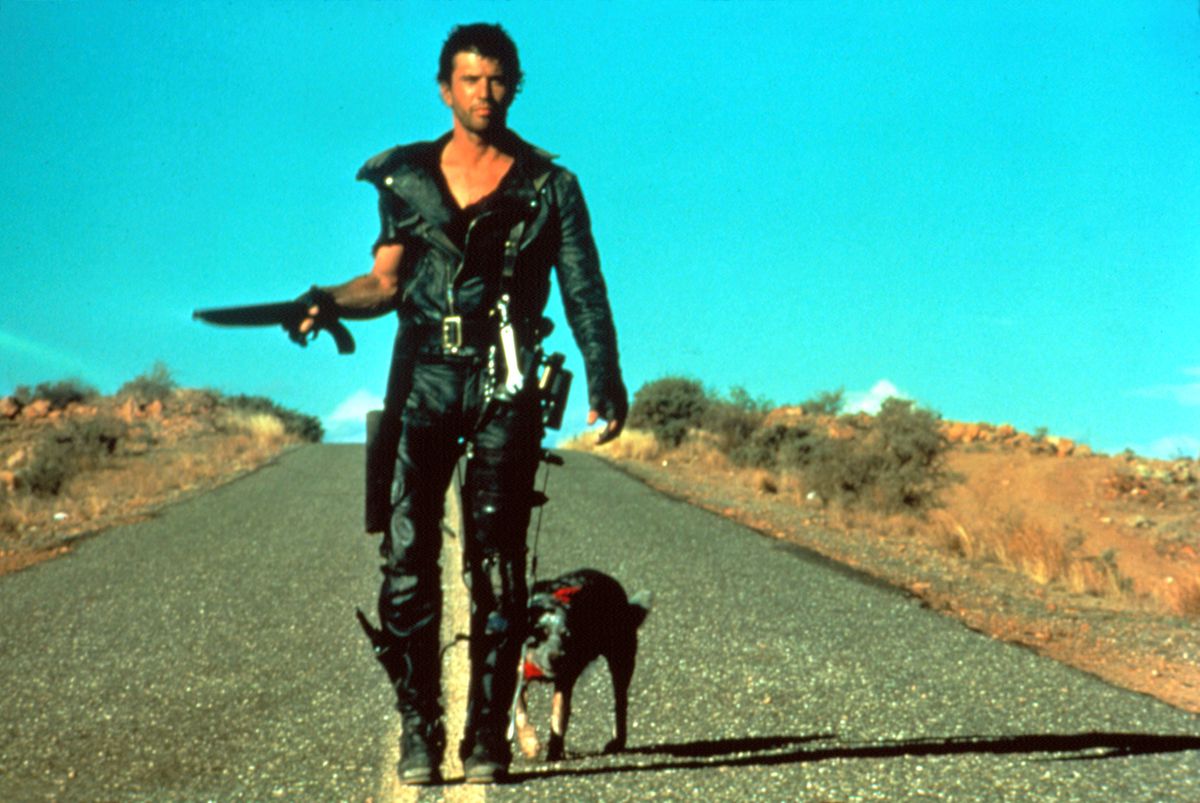 Mel Gibson som Mad Max, klädd i helt svart läder och med ett kort hagelgevär, går med en hund på en väg i Mad Max 2: The Road Warrior.