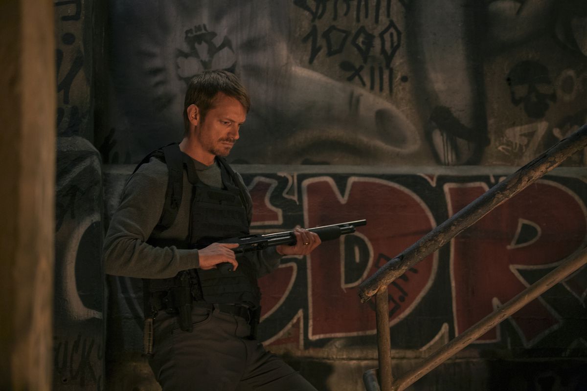 Joel Kinnaman, wearing body armor and wielding a shotgun, prepares to climb a staircase in Silent Night.