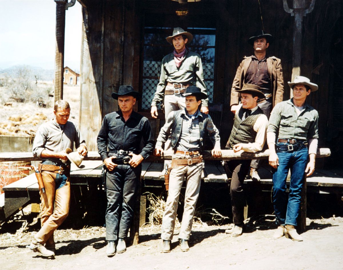 De sju cowboysna i The Magnificent Seven står runt varandra i solen