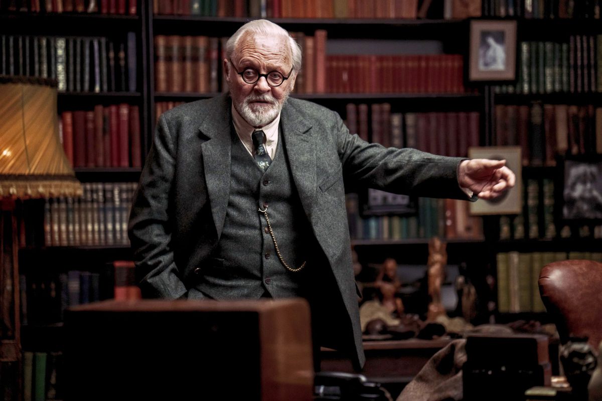 Freud stands in the middle of his book-filled study and raises his arm to make a point in Freud’s Last Session