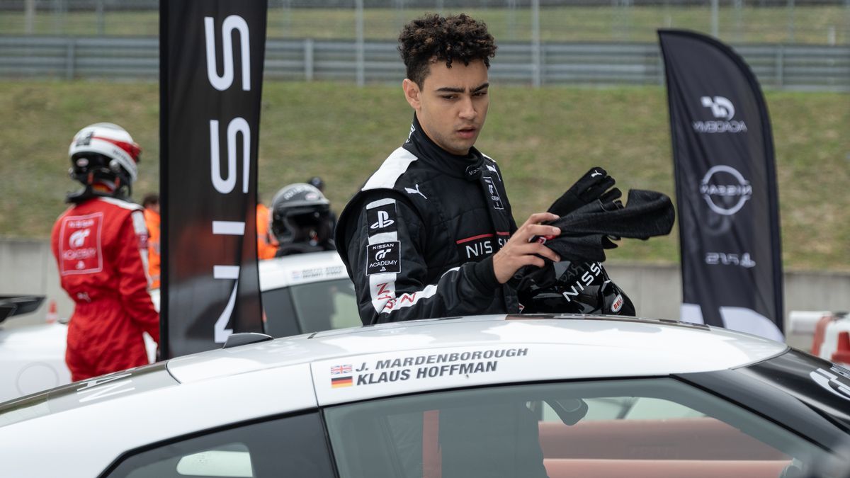 Archie Madekwe as Jann Mardenborough leans on the roof of his racing car in the Gran Turismo movie