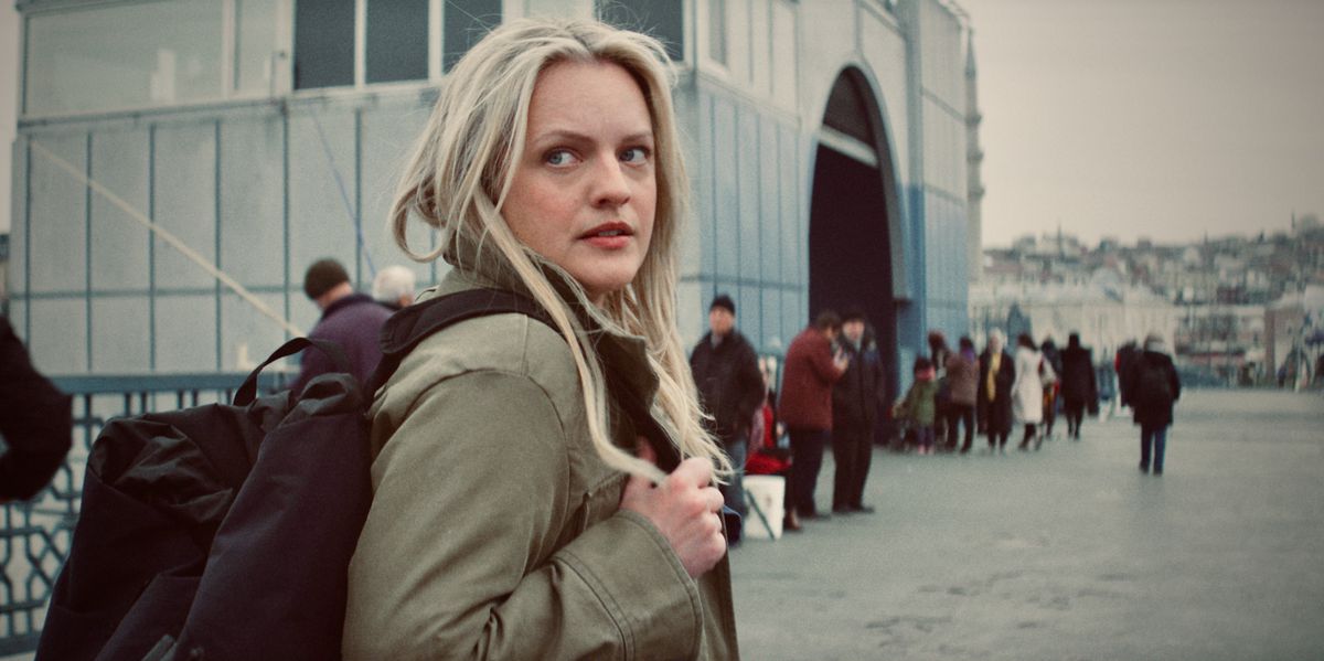 Elisabeth Moss looks over her shoulder while wearing a backpack in a cold environment in an image from The Veil