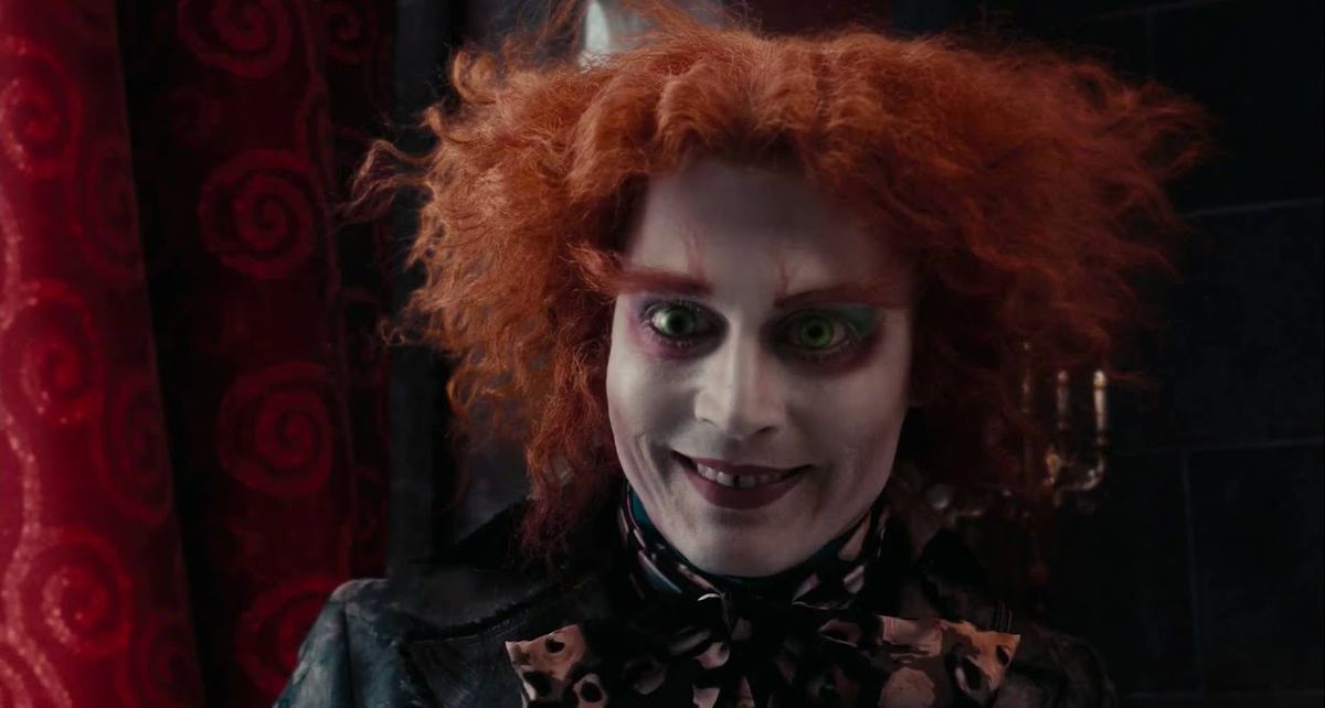 Johnny Depp as the Mad Hatter, with wild red wig, giant red eyebrows, white face paint, huge crimson circles under his eyes, and a manic grin, stares directly into the camera in 2010’s live-action Alice in Wonderland