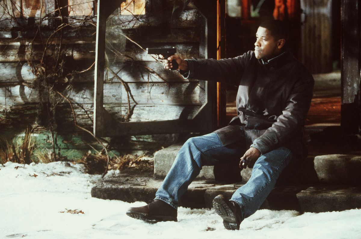 Denzel Washington, sitting on the steps in front of a log cabin, holds a gun in Fallen.