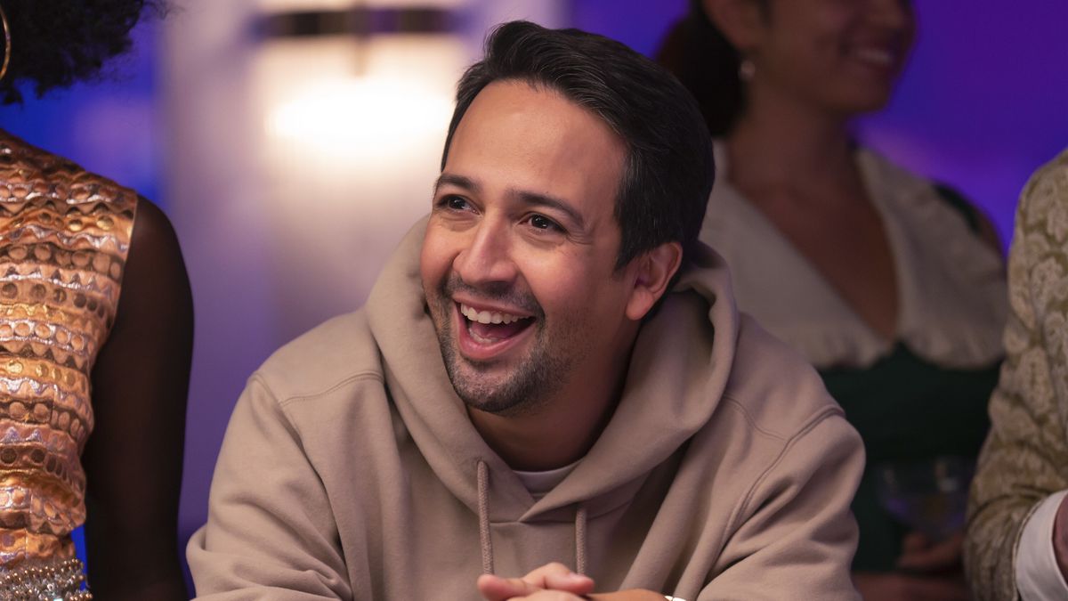 Lin-Manuel Miranda som Hermes, lutad över ett pokerbord med ett stort fånigt leende