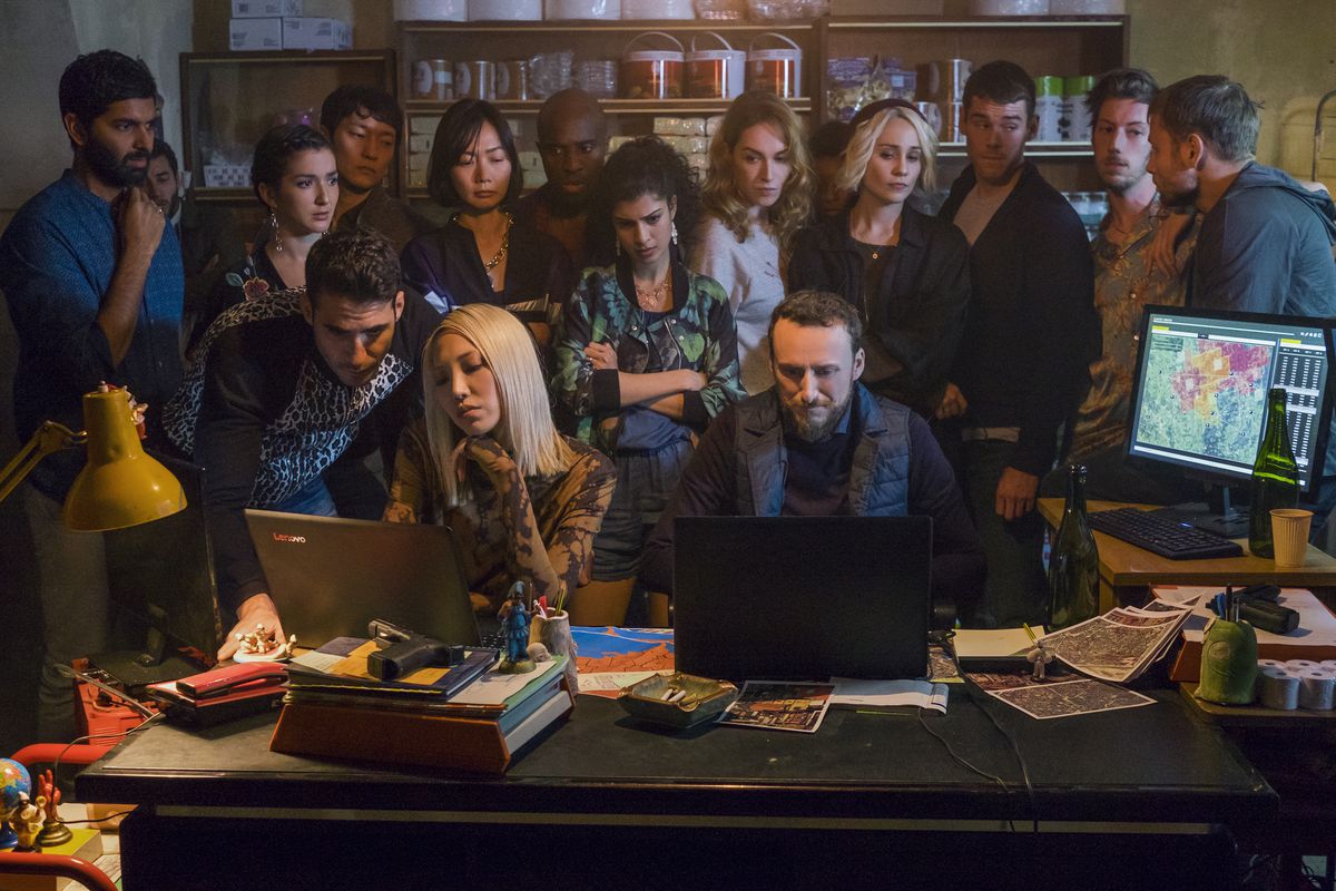 En grupp människor, inklusive huvudrollen i Sense8, står över axeln på två personer och skriver på bärbara datorer i Sense8.
