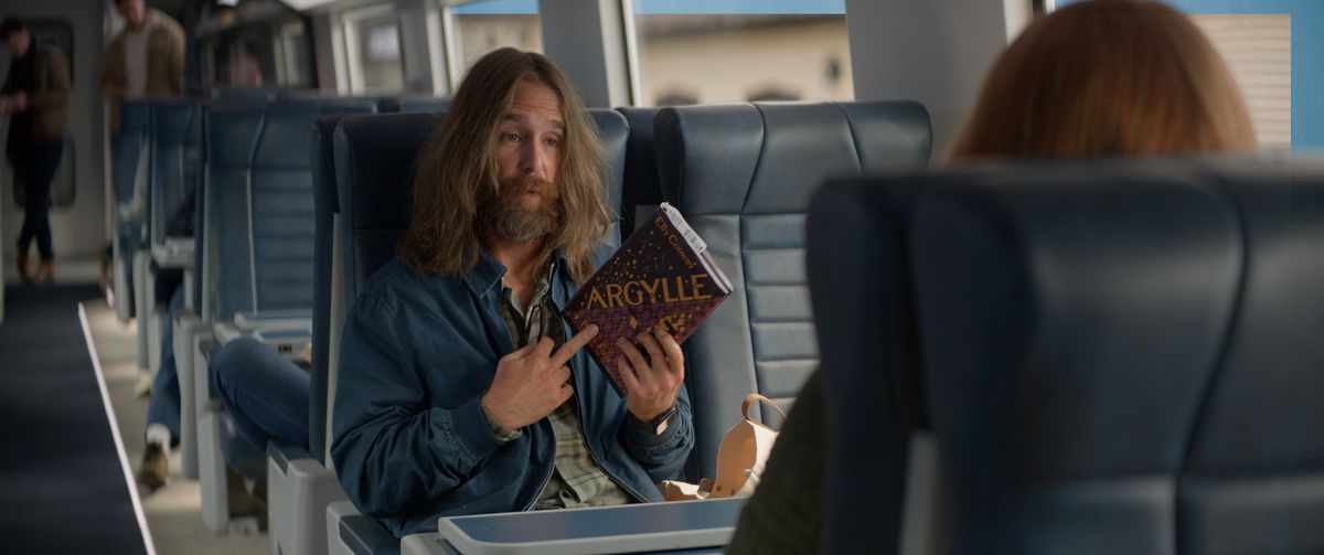 Sam Rockwell, med långt hår och skägg, har ett exemplar av boken Argylle av Elly Conway i filmen Argylle