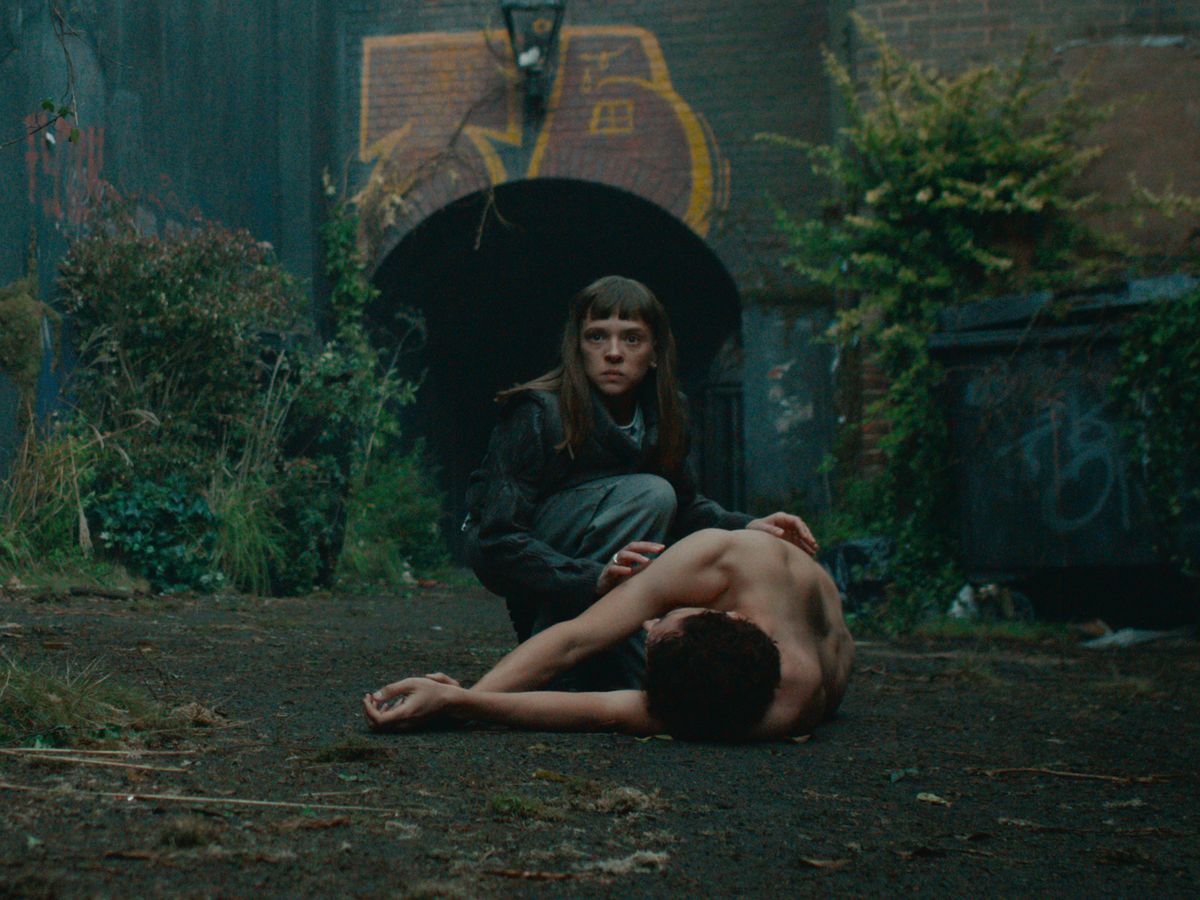 Shira Haas som DS Maplewood knäböjer bredvid en kropp på en innergård översvämmad av växter i Bodies.