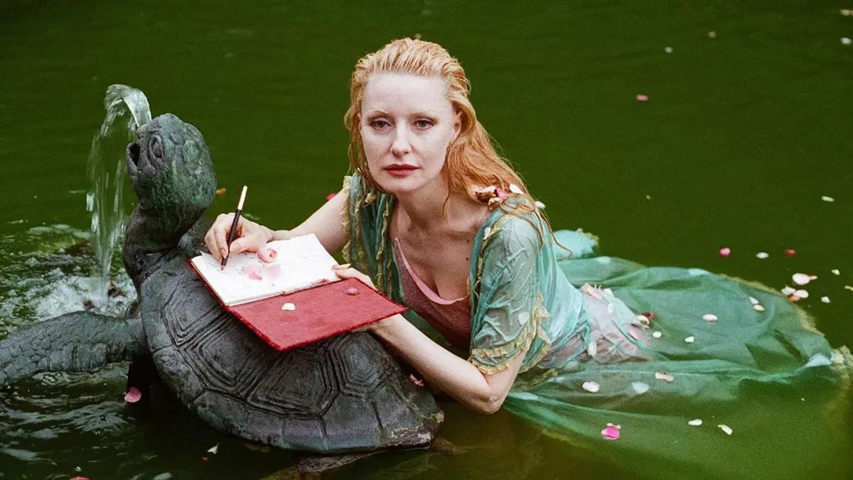 Foto Shere Hite som ligger i en vattenpöl och skriver i en röd dagbok ovanpå en stensköldpaddsfontän i dokumentären 