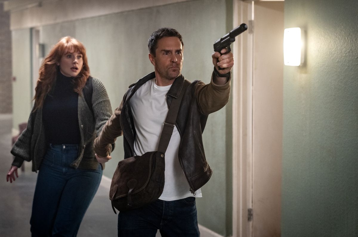 Sam Rockwell, viftande med en tystad pistol, leder en rädd utseende Bryce Dallas Howard nerför en korridor i Argylle