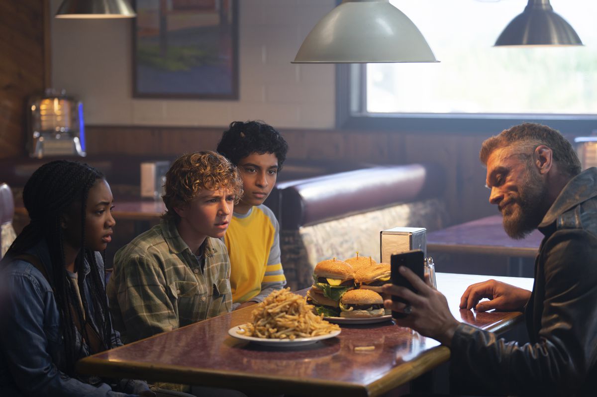Annabeth, Percy och Grover äter cheeseburgare med Ares på en smutsig restaurang vid vägen