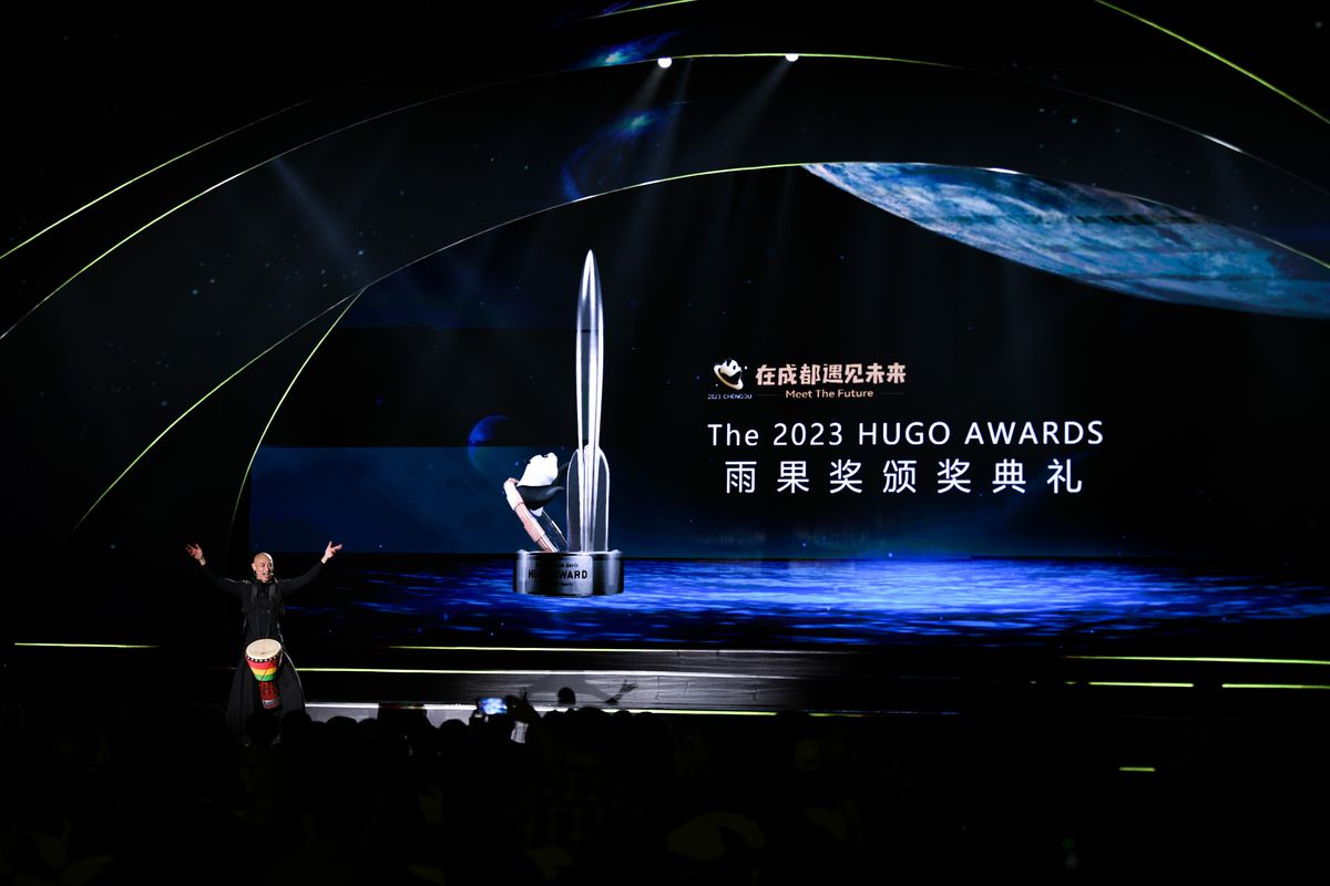 A man stands behind a podium with arms raised on stage at the award ceremony for the 2023 Hugo Awards in Chengdu, China. 