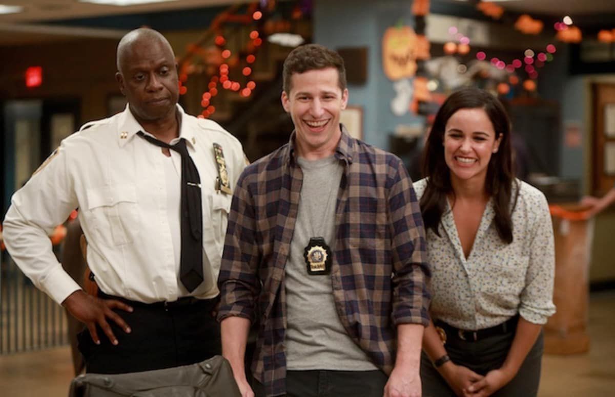 Andy Samberg and Melissa Fumero laugh while Andre Braugher glowers in Brooklyn Nine-Nine.